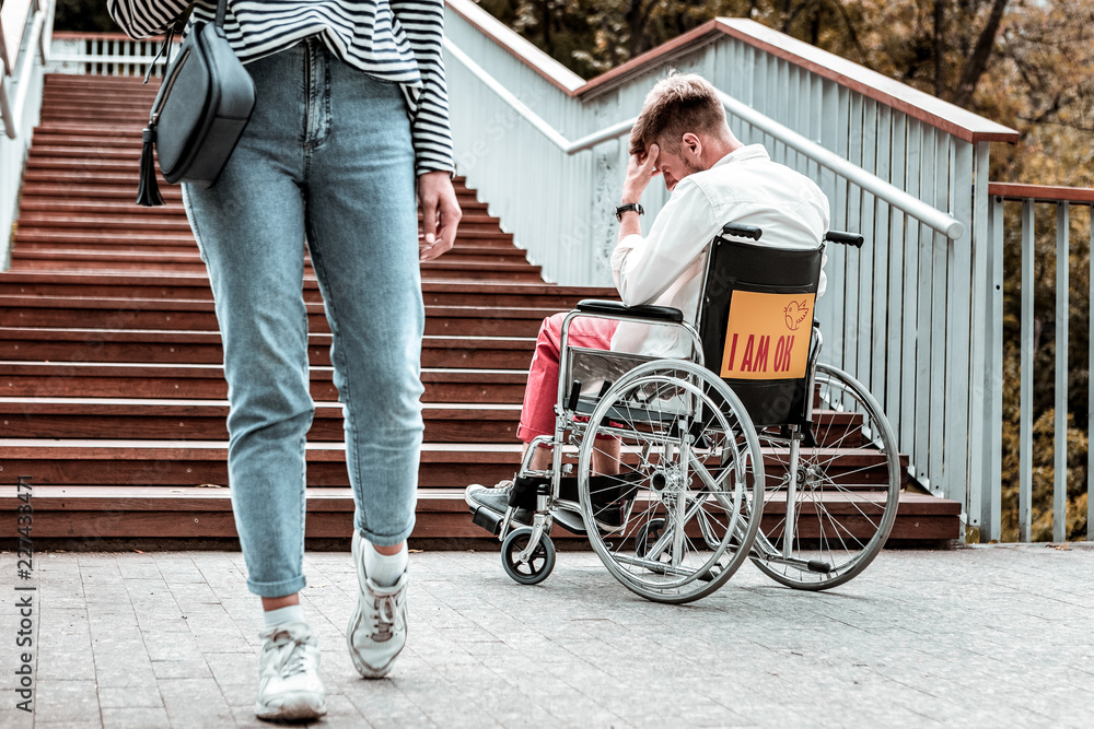 No attention. Young woman walking and paying no attention to the sad disabled man sitting in the