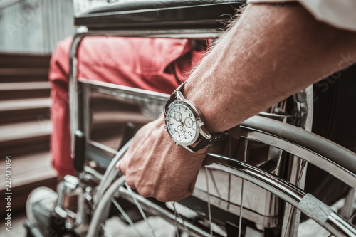 Time. Close up of young person putting hand on the wheel while sitting in the wheelchair