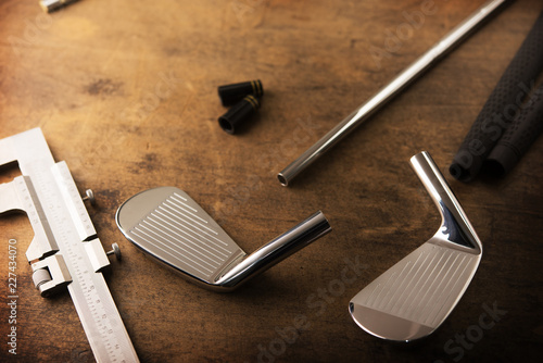 Assembling golf clubs or golf club making. Iron head, steel shaft, ferrule and grip on a well used work bench. Shot in impression-like surreal color with low key shadows. Shallow depth of field. photo