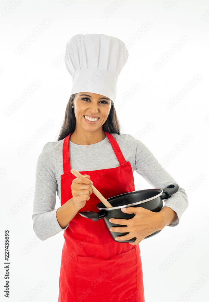 Beautiful happy young woman chef holding a wooden spoon and a pot with red apron and white hat Beautiful happy young woman chef holding a wooden spoon and a pot with red apron and white hat