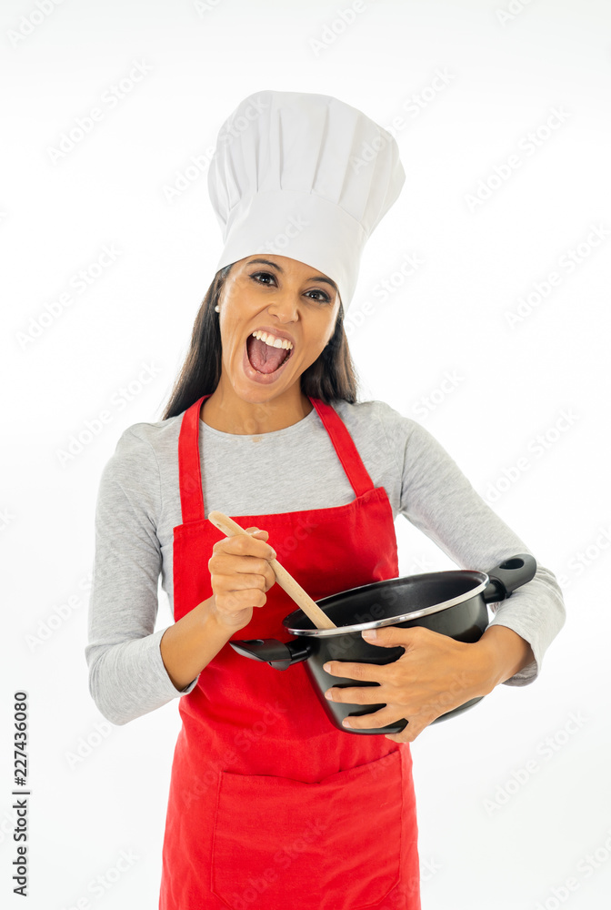 Beautiful happy young woman chef holding a wooden spoon and a pot with red apron and white hat Beautiful happy young woman chef holding a wooden spoon and a pot with red apron and white hat