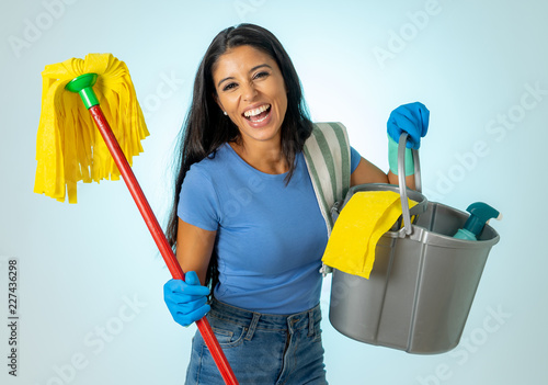 Young attractive woman holding cleaning tools and products in bucket isolated on blue background photo