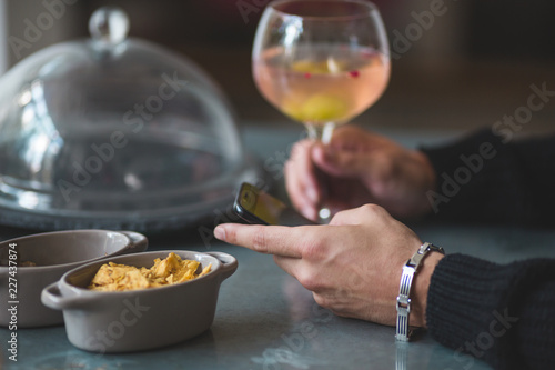Close-up of a male hand holding mobile phone with one hand and glass of alcohol with other hand