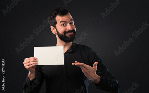 Handsome man with beard holding an empty placard on black background