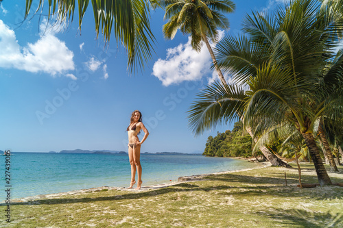 Beautiful woman in bikini on tropical beach. Portrait of happy young woman at sea. Brunette tanned girl in swimwear enjoying and walking on beach.
