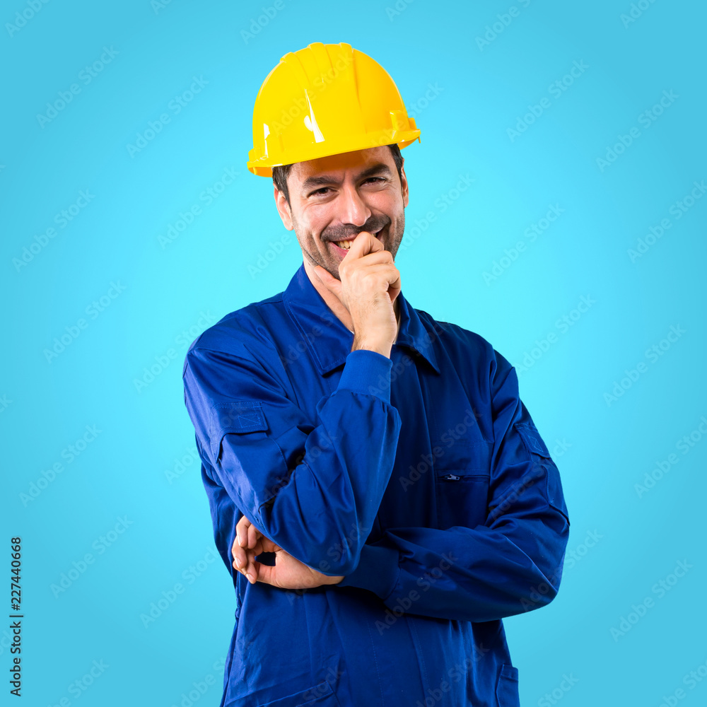 Young workman with helmet smiling with a sweet expression on blue background Young workman with helmet smiling with a sweet expression on blue background