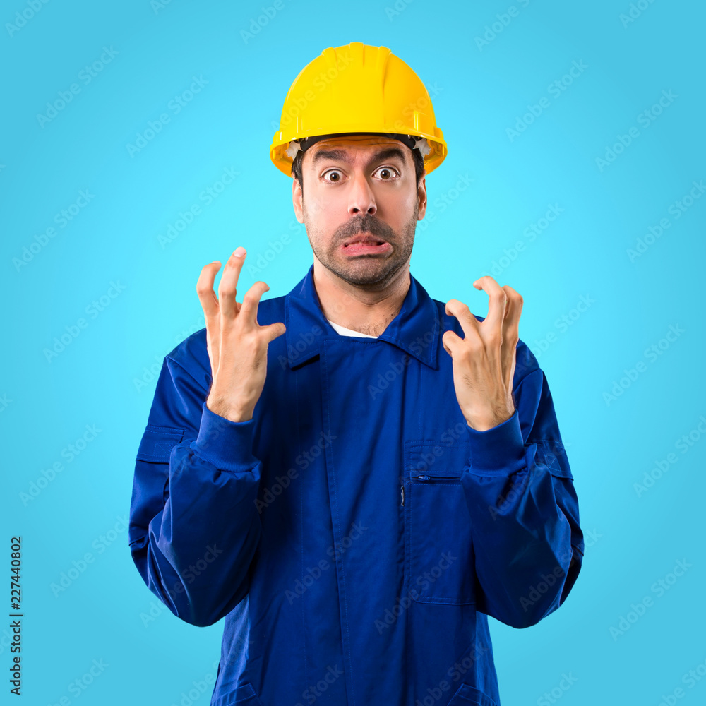 Young workman with helmet annoyed angry in furious gesture. Negative expression on blue background Young workman with helmet annoyed angry in furious gesture. Negative expression on blue background
