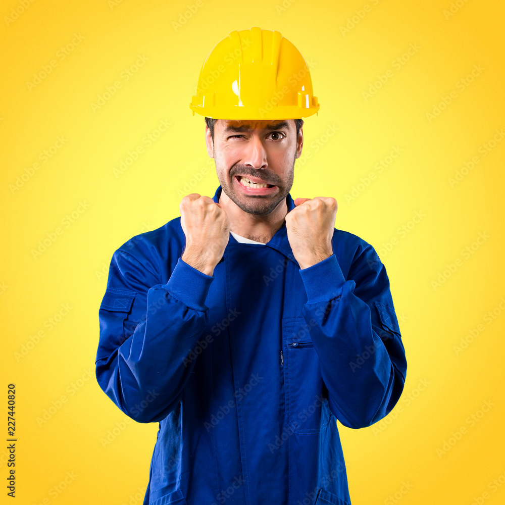Young workman with helmet annoyed angry in furious gesture. Frustrated by a bad situation on yellow background