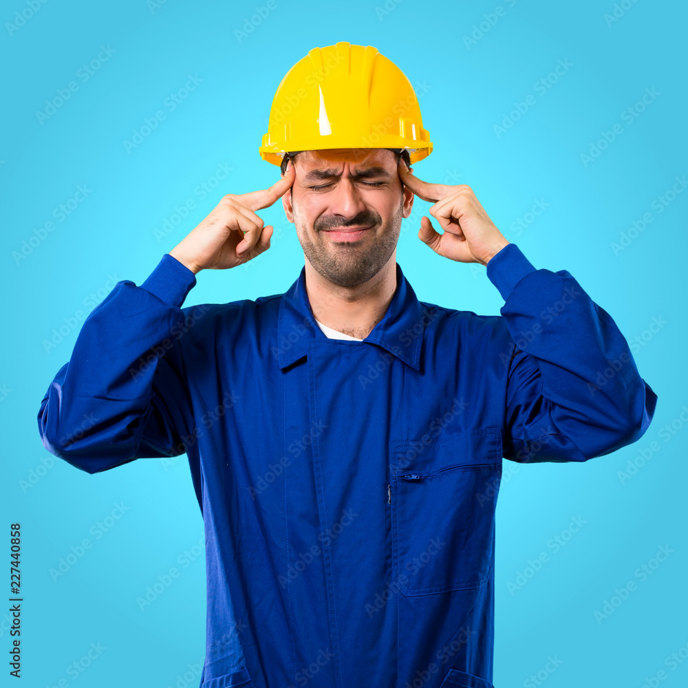Young workman with helmet unhappy and frustrated with something. Negative facial expression on blue background