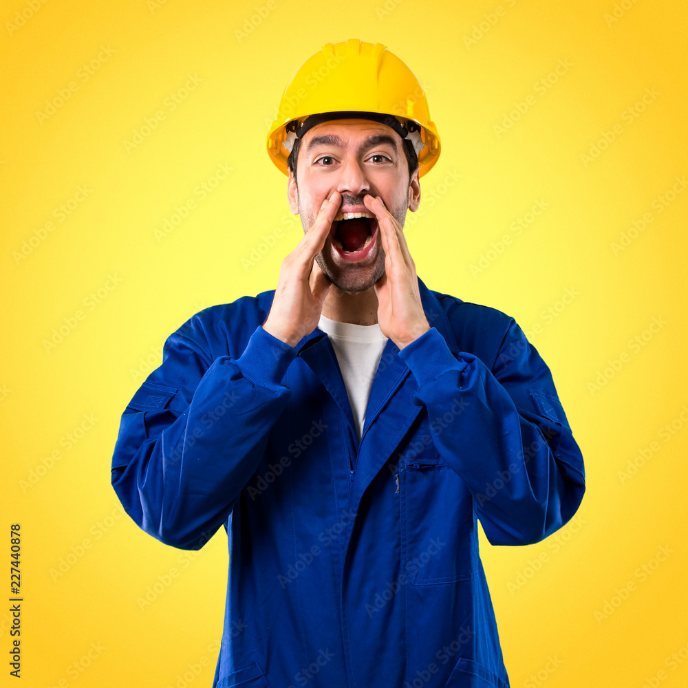 Young workman with helmet shouting with mouth wide open and announcing something on yellow background Young workman with helmet shouting with mouth wide open and announcing something on yellow background