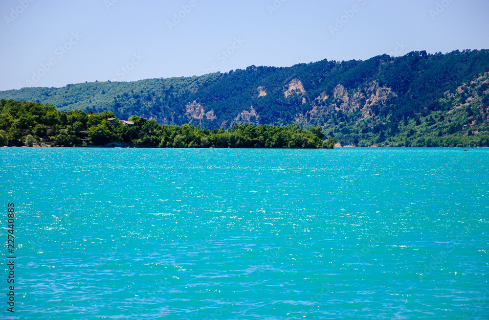 Beautiful view of St. Croix lake in Verdon and the forested hills of the coastline. (Provence, France) Sunlight on the water surface. 