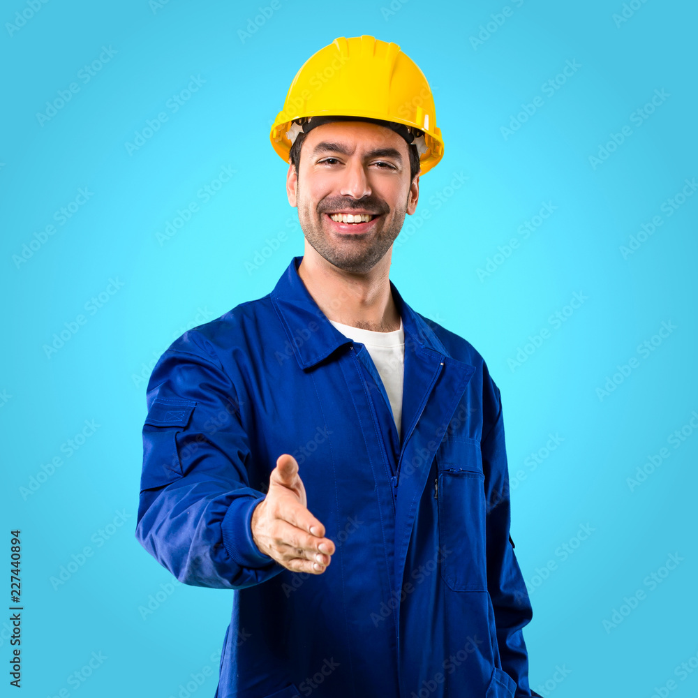 Young workman with helmet shaking hands for closing a good deal on blue background Young workman with helmet shaking hands for closing a good deal on blue background