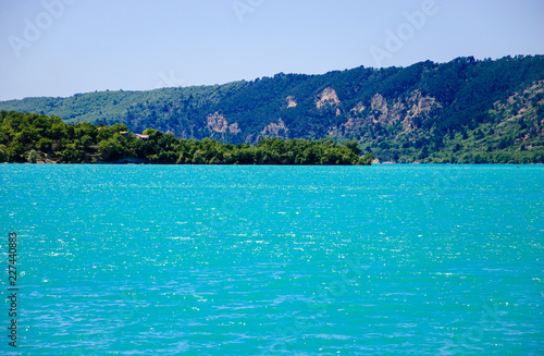 Beautiful view of St. Croix lake in Verdon and the forested hills of the coastline. (Provence, France) Sunlight on the water surface.  © Elena Dijour