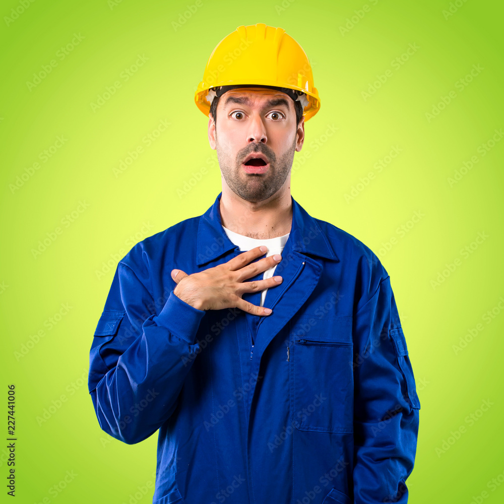 Young workman with helmet surprised and shocked while looking right. Expressive facial emotion on green background Young workman with helmet surprised and shocked while looking right. Expressive facial emotion on green background