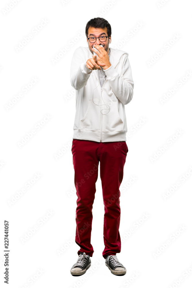 A full-length shot of a Man with glasses and listening music pointing with finger at someone and laughing a lot while covering mouth on white background A full-length shot of a Man with glasses and listening music pointing with finger at someone and laughing a lot while covering mouth on white background