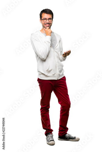 A full-length shot of a Man with glasses and listening music smiling with a sweet expression on white background © luismolinero