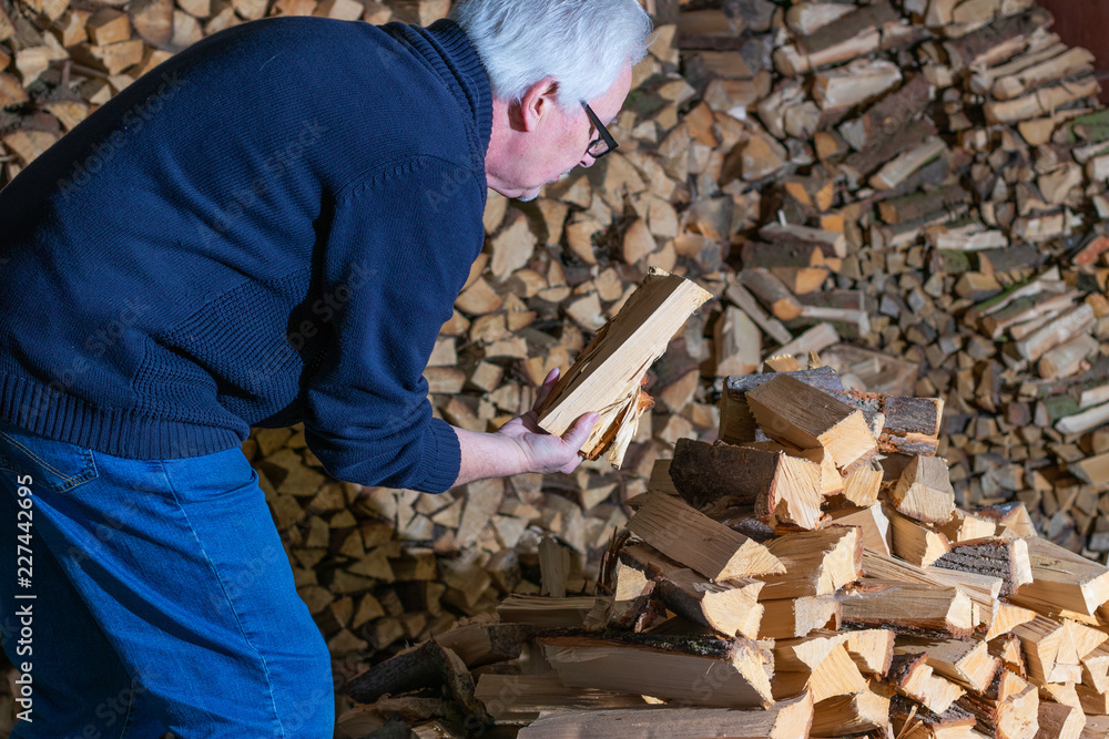 Mann stapelt Kaminholz für den Kaminofen im Winter Mann stapelt Kaminholz für den Kaminofen im Winter