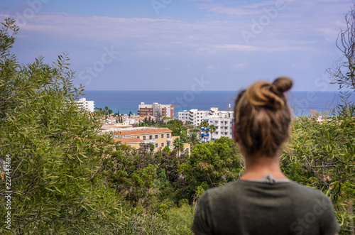 Fototapeta Naklejka Na Ścianę i Meble -  A woman stares into the distance to the sea horizon and the city in front of him