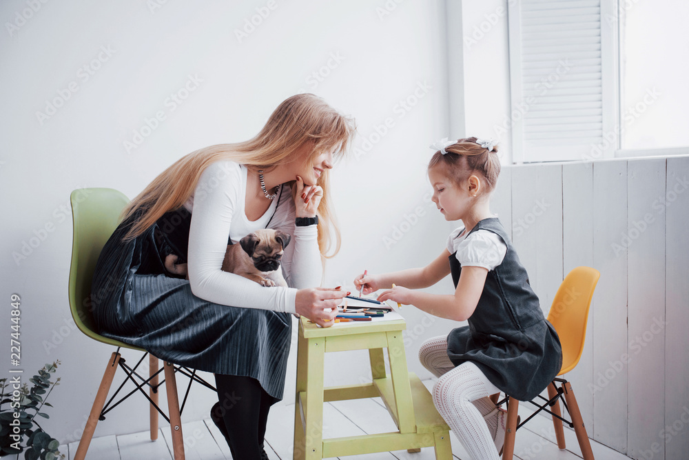 mother and child daughter draws are engaged in creativity in kindergarten. small pug with them mother and child daughter draws are engaged in creativity in kindergarten. small pug with them
