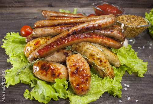 Assorted grilled sausages on lettuce leaves on a wooden table. Delicious food for gourmets, lovers of sausages and beer.