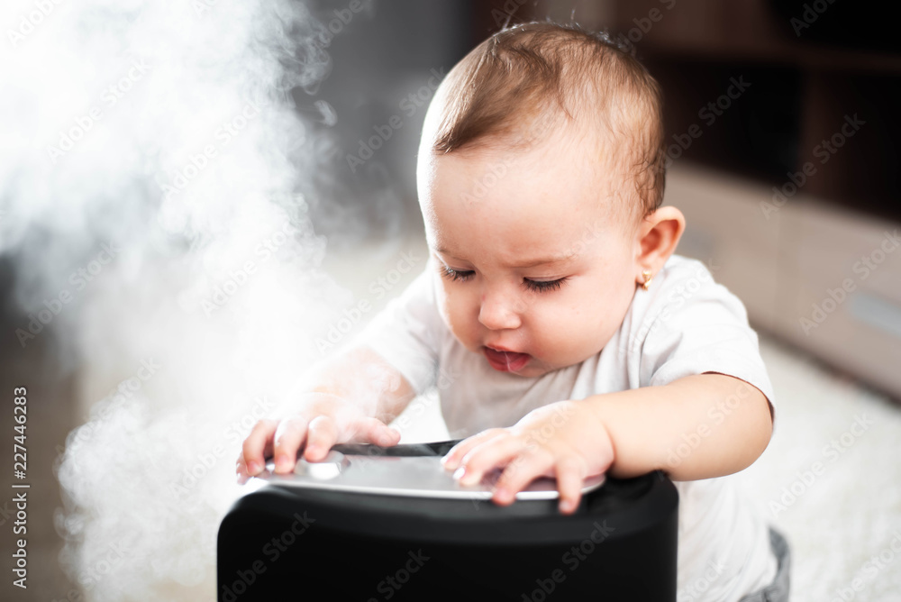 Little baby looks at the humidifier. Moisture in the house concept Little baby looks at the humidifier. Moisture in the house concept
