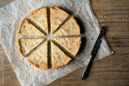 Zitronenkuchen in gleich große Stücke geschnitten symmetrisch platziert auf weißem Backpapier und braunem Untergrund von oben bei Tageslicht fotografiert
