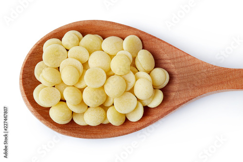 Organic cacao butter buttons (wafers) in wooden spoon isolated on white background. Top view