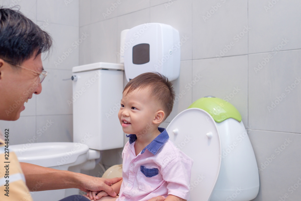 Father teaching son to use public toilet for kids in family restroom