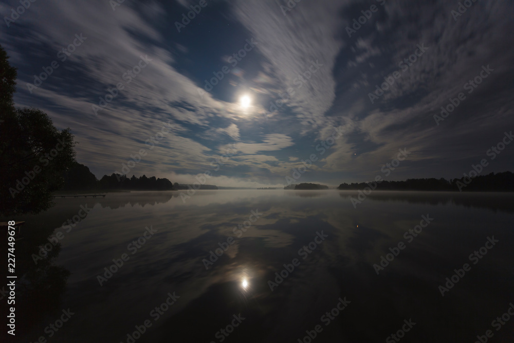Clouds in the night over the lake lit by full moon, long exposure shot