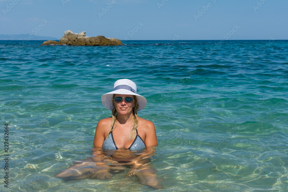 the girl sits in the sea with a hat and sunglasses