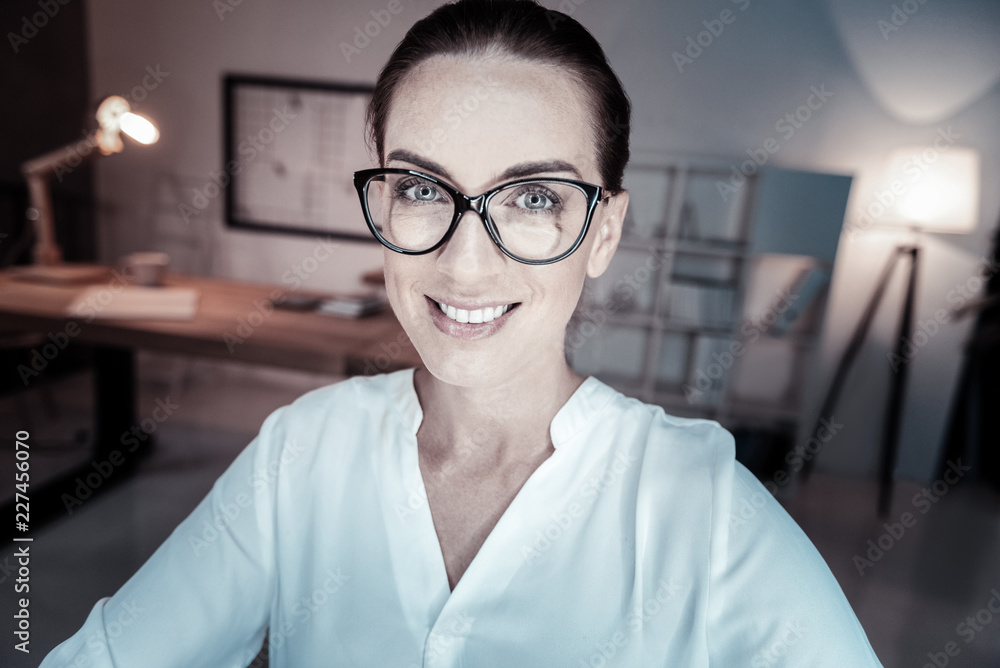 Happy to be here. Pretty office worker smiling while looking at camera and standing on the foreground Happy to be here. Pretty office worker smiling while looking at camera and standing on the foreground