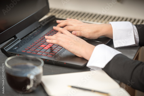 Wallpaper Mural a woman's hand on a black-and-red laptop keyboard, which lies on a dark table, next to coffee and an open notebook Torontodigital.ca