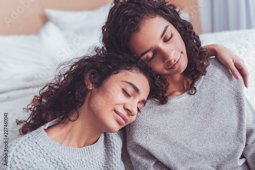 Feeling relieved. Two curly-haired cheerful cousins feeling relieved after their personal conversation while sitting near double bed