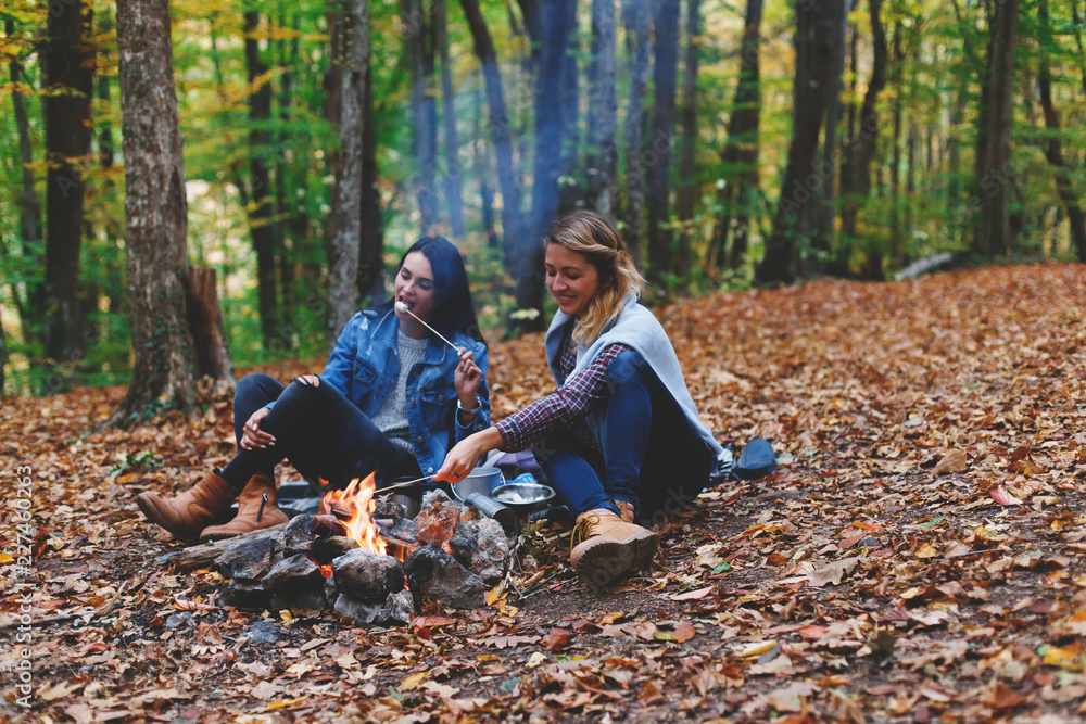 Two young girls friends roasting sweet marshmallow on a fire in the evening in the autumn forest. Two young girls friends roasting sweet marshmallow on a fire in the evening in the autumn forest.
