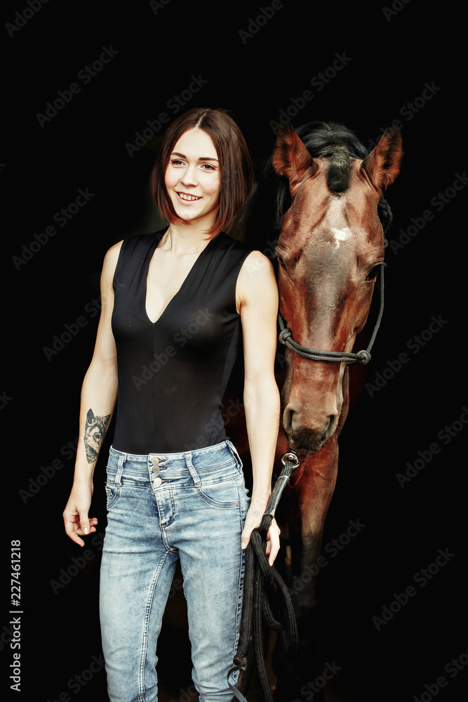 Fototapeta premium Portrait of smiling pretty woman standing by horse on the black background. Isolate