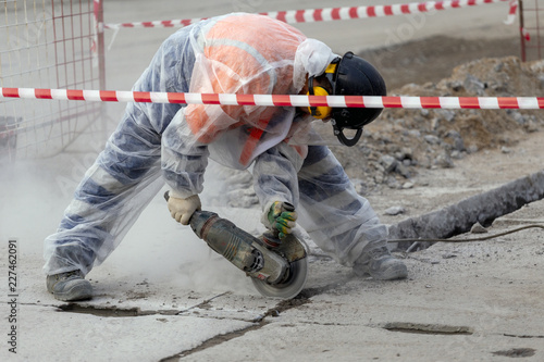 worker catching and using electric cutting machine tool to cut concrete floor with dirty dust spreading in air,