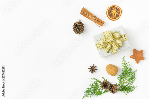 Gift box wrapped in silver polka dot paper golden ribbon bow pine cones juniper nuts cinnamon on solid white background. New Year presents holiday preparations. Minimalist poster banner mockup