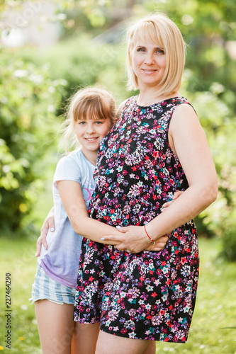Mother and Daughter. Beautiful pregnant woman in short floral maternity dress and child looking to the camera and smiling