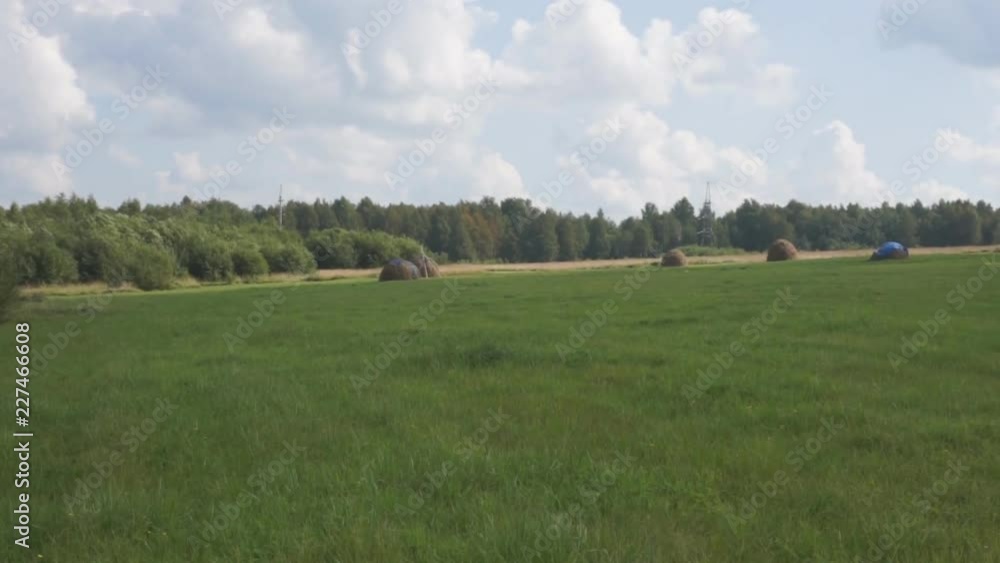 A tractor is slowly driving a tractor on a mown grass. The day is sunny and beautiful. It is summer time. A tractor is slowly driving a tractor on a mown grass. The day is sunny and beautiful. It is summer time.