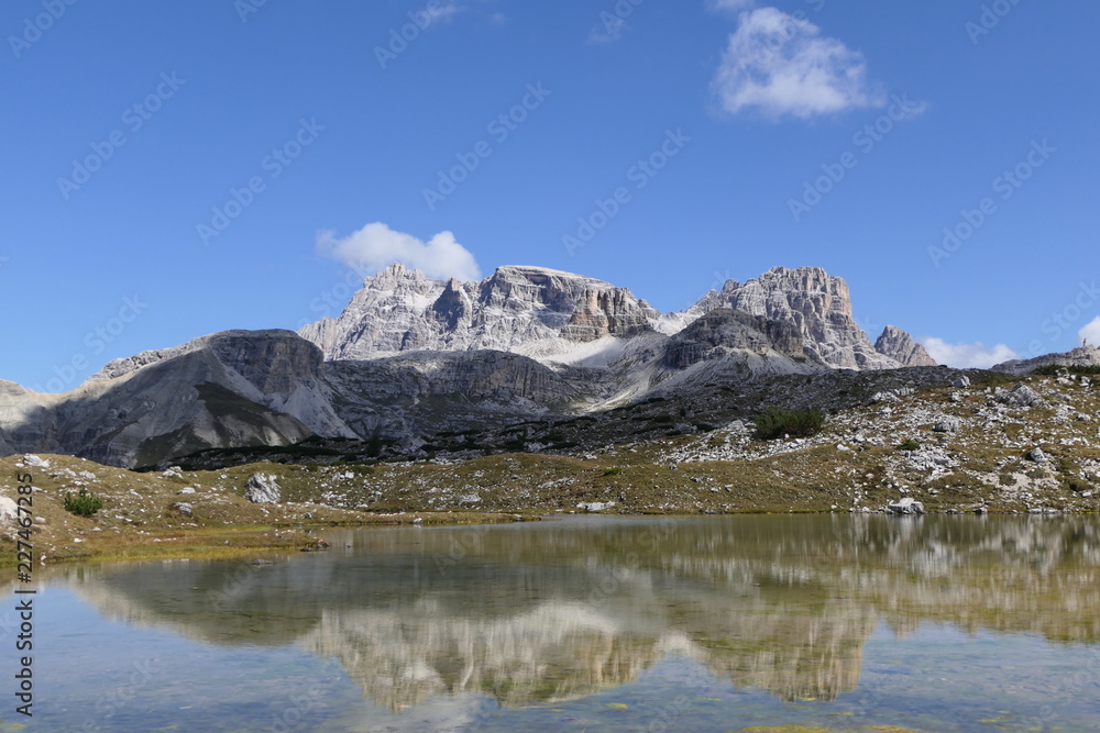 Mountains and lakes in a wonderful landscape. A mountain range is reflected in a lake. Blue sky with some clouds casting their shadows on the hills. No person is visible.