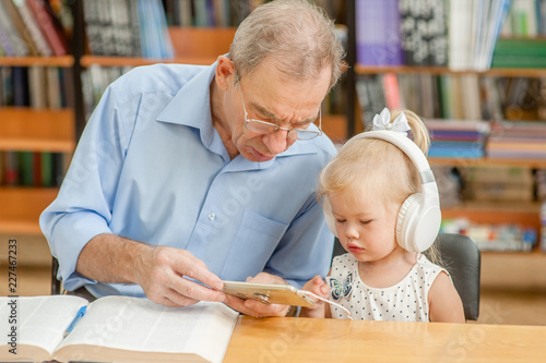 elderly man with a little girl is using a smartphone in the library