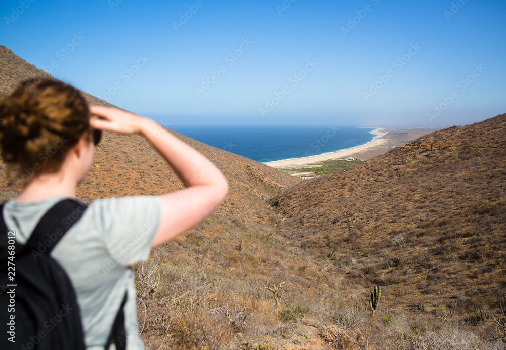 Woman overlooking ocean beach from desert hiking trail - horizontal