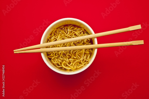 top view of cup of instant noodles and wooden chopsticks over gradient red background