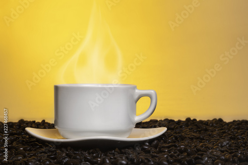 Cup of fresh steaming hot coffee on top of roasted coffee beans.