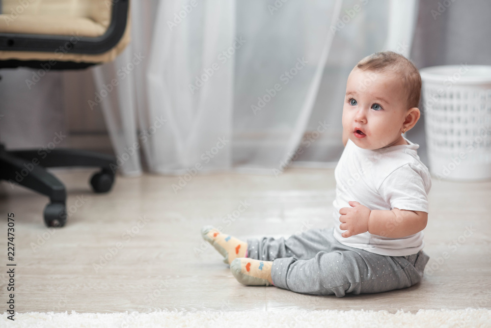 Naklejka premium A little girl sitting on a laminate flooring in a bright room, happy