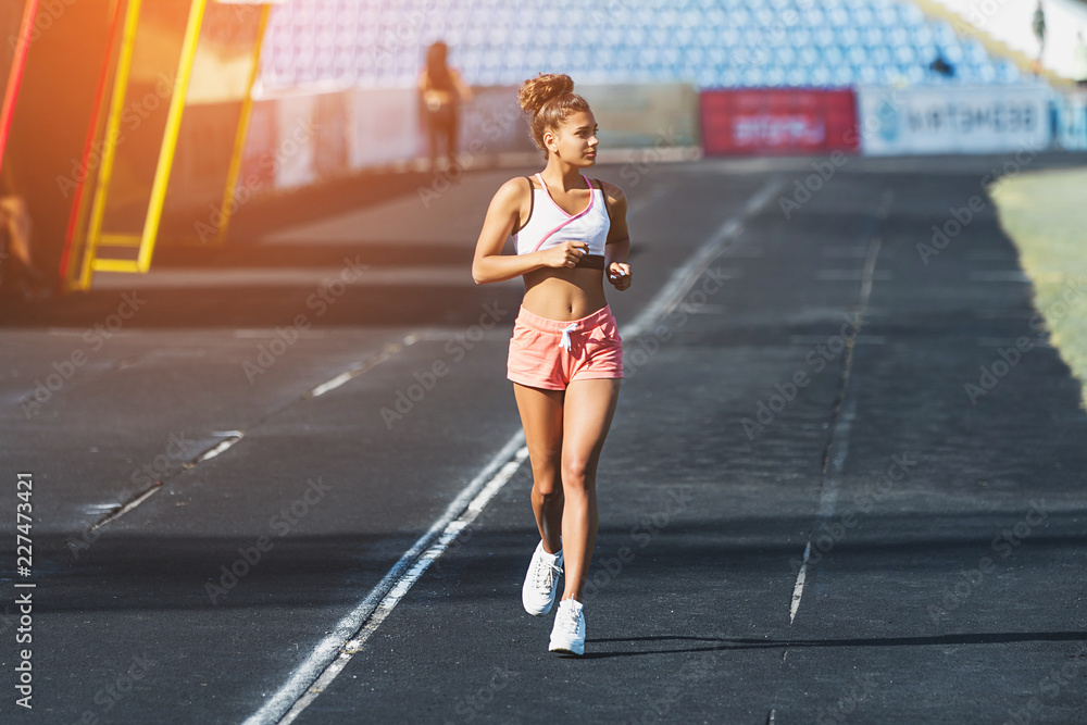 Young woman running on racetrack during training session. Female runner practicing on athletics race track. Sunshine background
