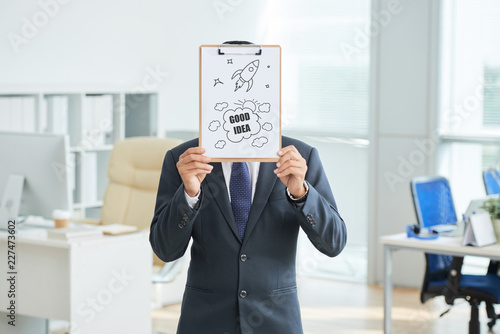 Portrait of businessman in suit standing and holding clipboard with good idea in front of his face