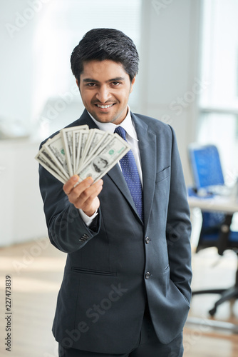 Portrait of happy office worker holding wad of dollar currencies while standing at office
