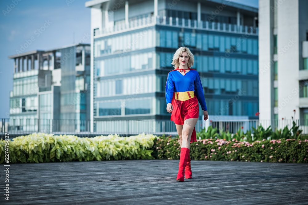 Full-length portrait of young attractive Caucasian woman in sexy superwoman costume walking down the street and looking at camera