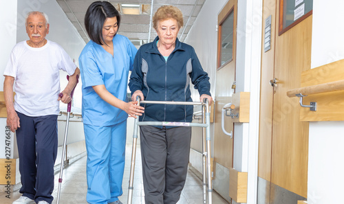 Asian doctor helping elder woman with walker and man in hospital aisle photo